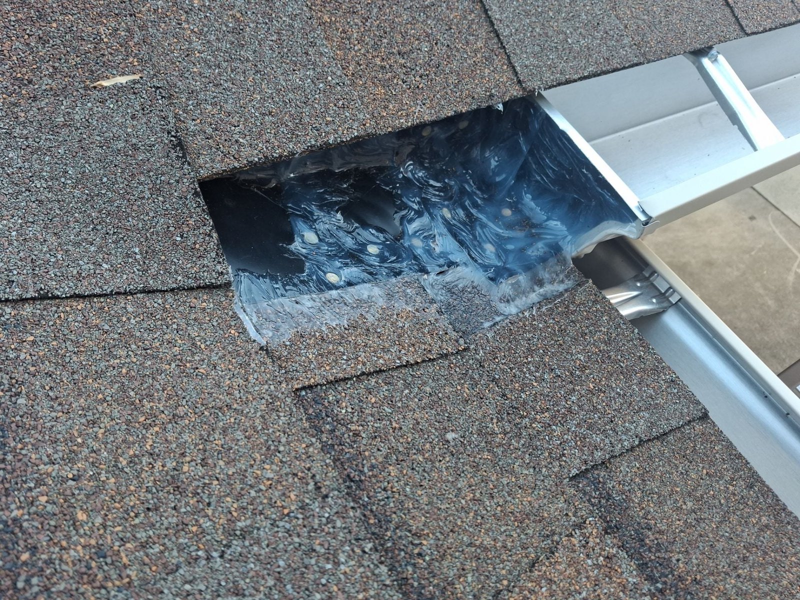 Field example showing patch metal, roof penetrations, and heavy sealant at a roof-edge water path on a system not installed by McCloud Gutter.